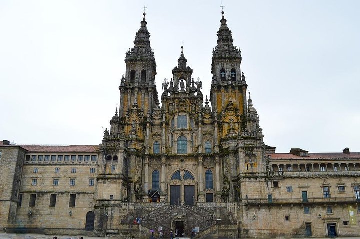 Pilgrims crossing a pale sanctuary plaza under an open sky, contrasted with granite cathedral stonework